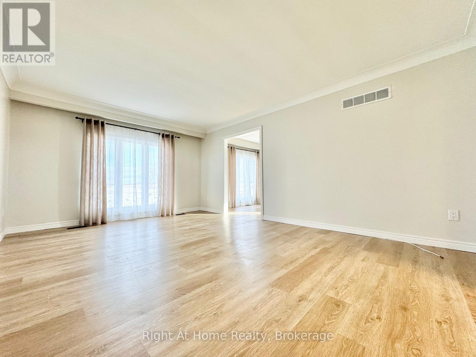 A spacious room with wooden flooring and a large window with curtains.