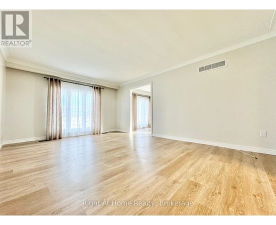 A spacious room with wooden flooring and a large window with curtains.