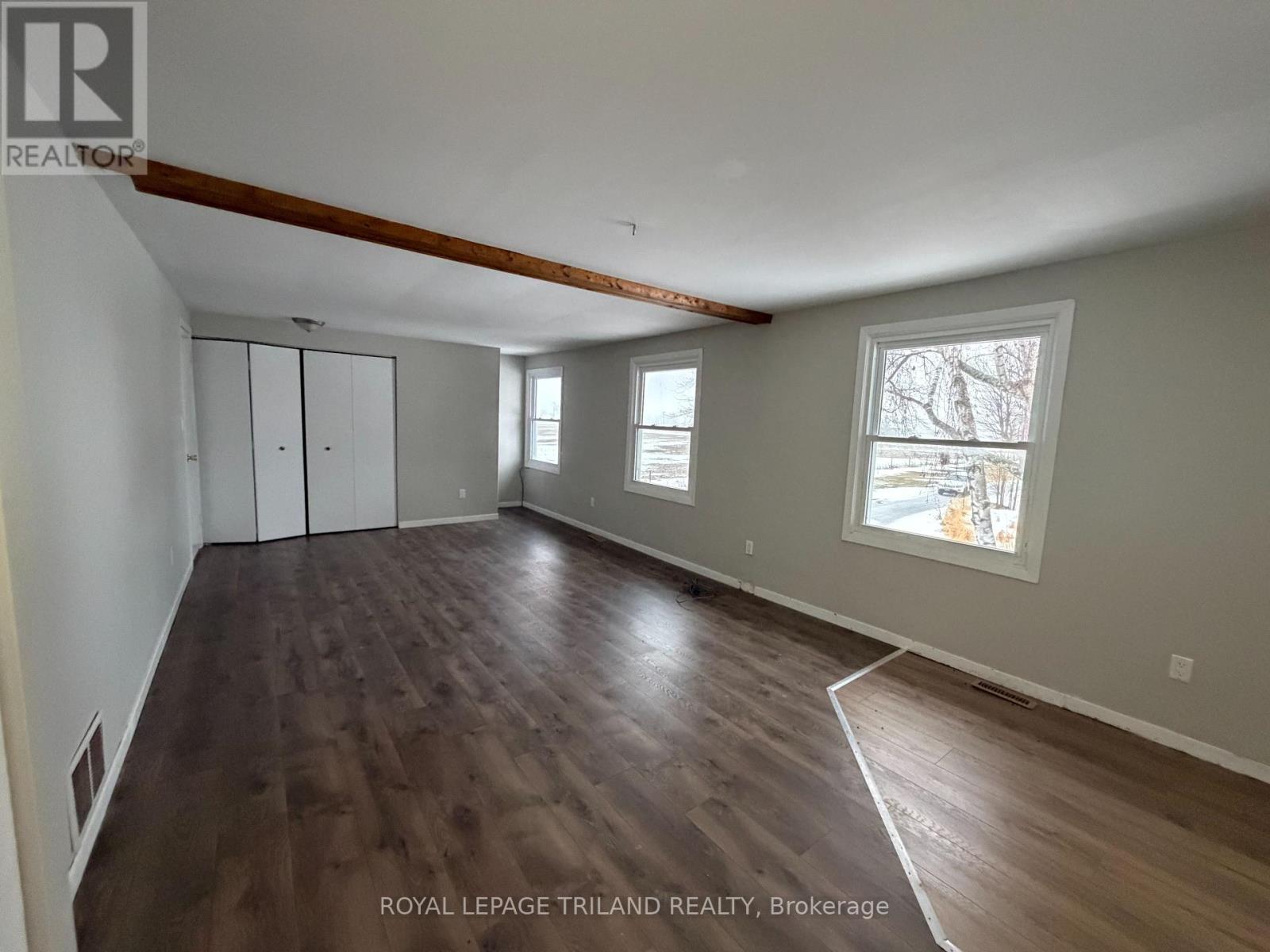 A spacious room with wood flooring and a large window.