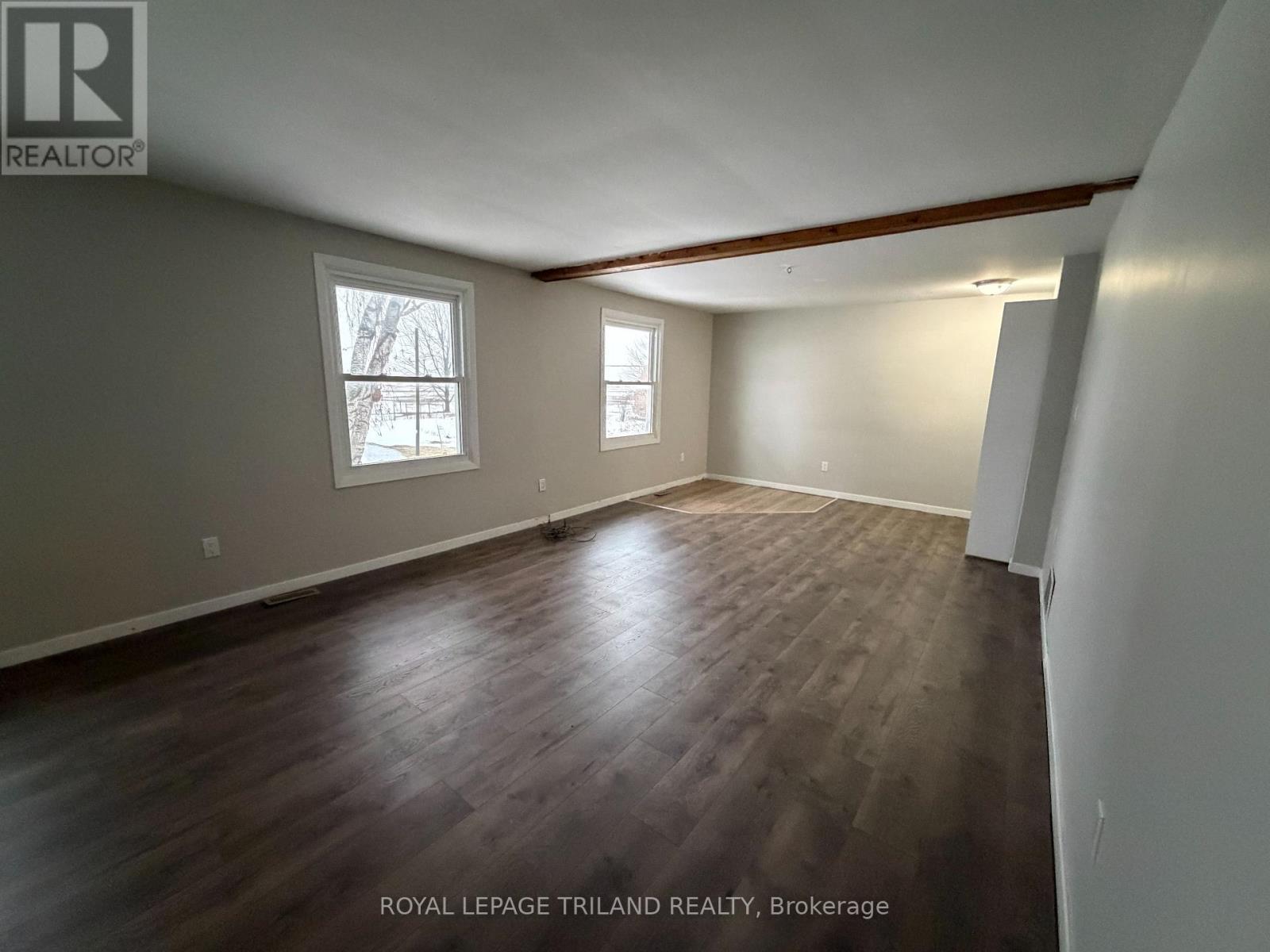 A spacious room with wooden flooring and two windows.
