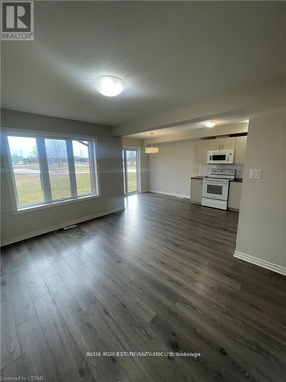 A spacious room with wood flooring and a kitchenette in the corner.