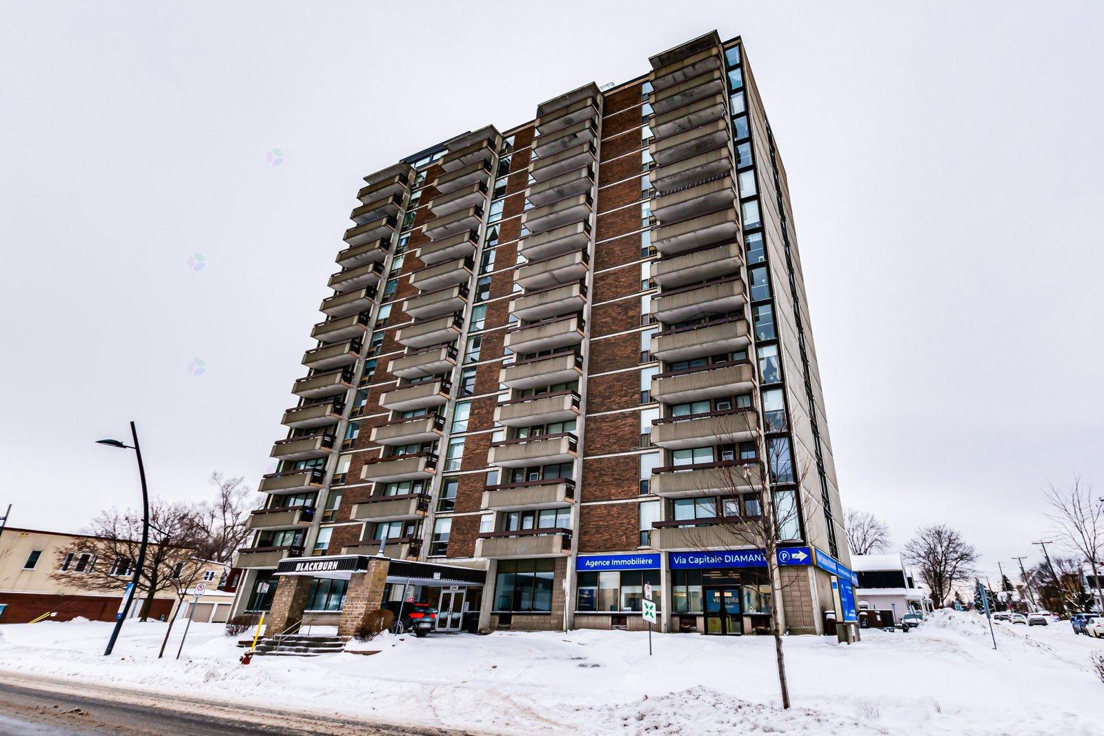 A tall apartment building with a blue awning in front.