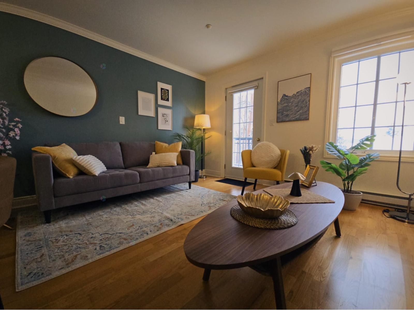 A living room with a grey couch and a round mirror on the wall.
