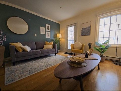 A living room with a grey couch and a round mirror on the wall.