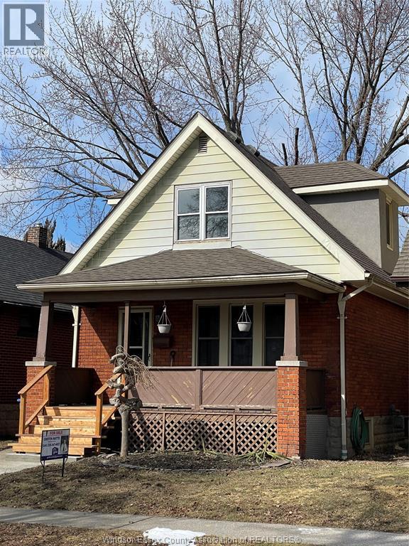 A house with a brown brick chimney and a porch with a wooden railing.
