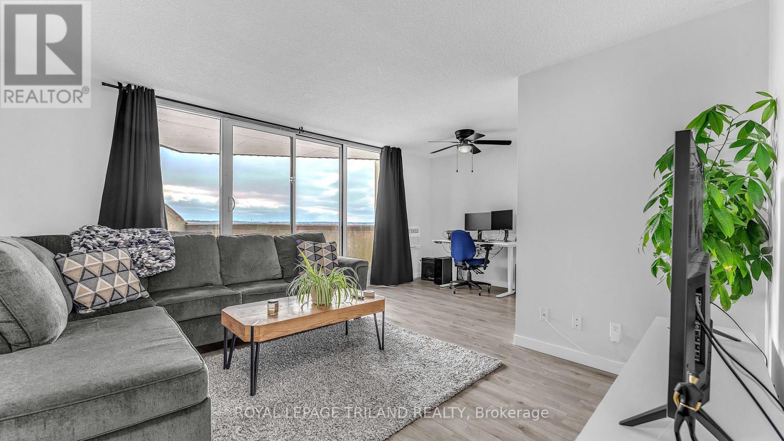 A living room with a grey couch, a wooden coffee table, and a large window with a view of the sky.