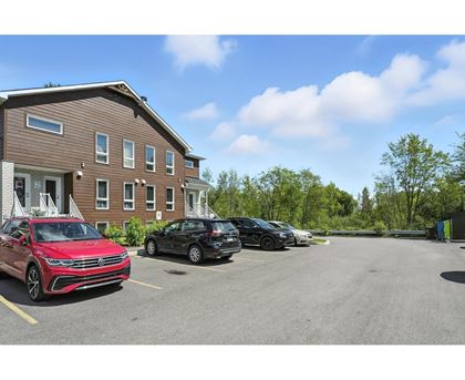 A red car is parked in a parking lot in front of a brown building.