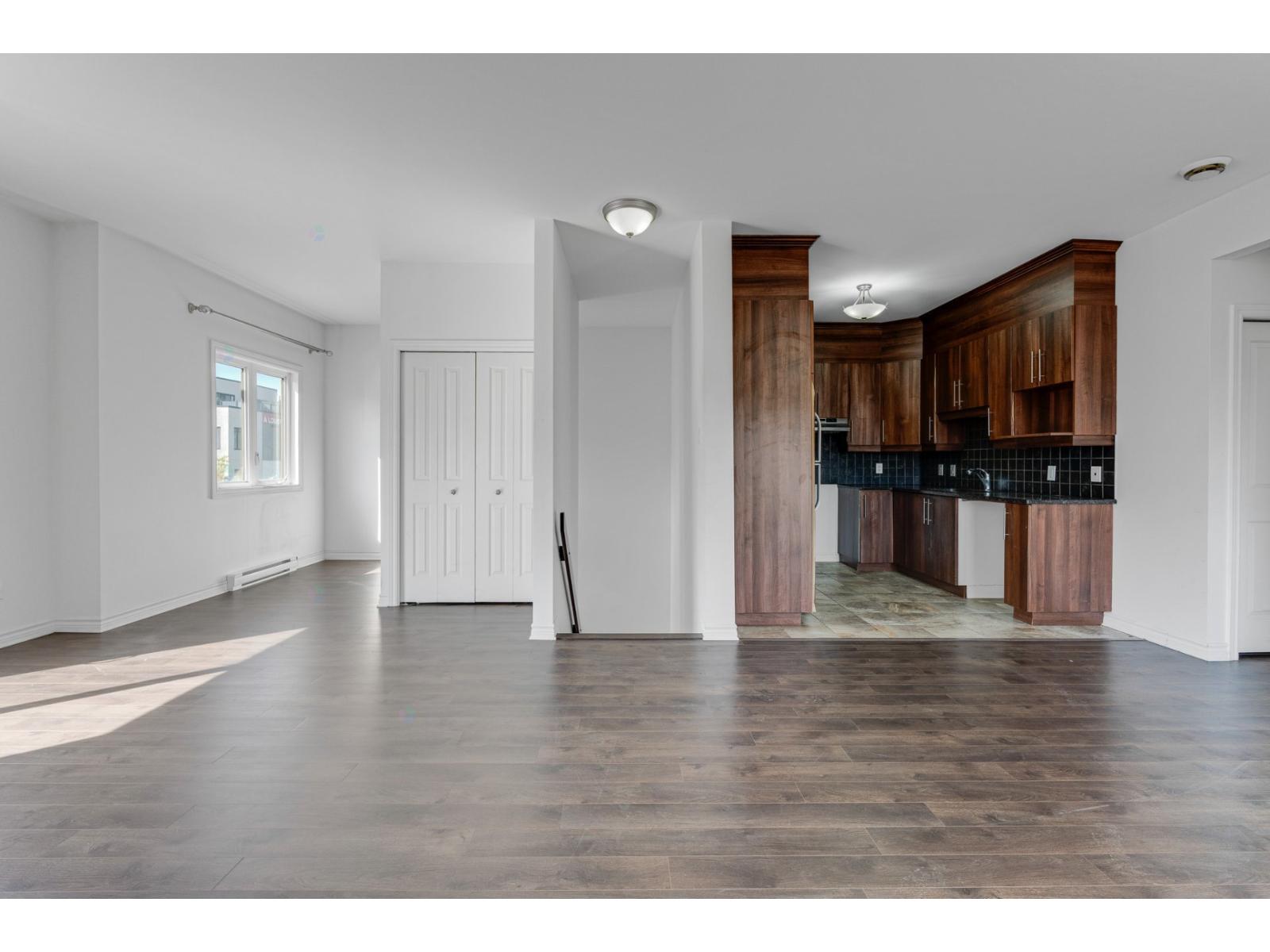 A kitchen with dark wood cabinets and a black countertop is seen from the living room.