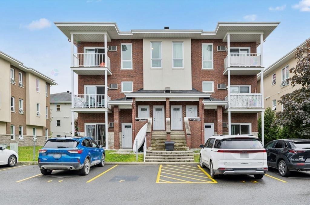 A blue car is parked in a parking lot in front of a two-story apartment building.