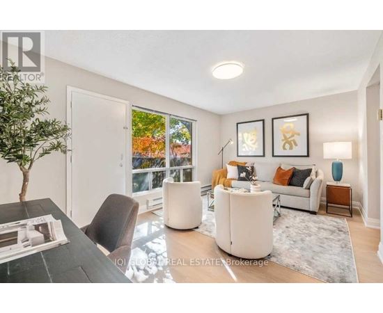 A living room with a white couch, a black chair, and a coffee table with a plant on it.