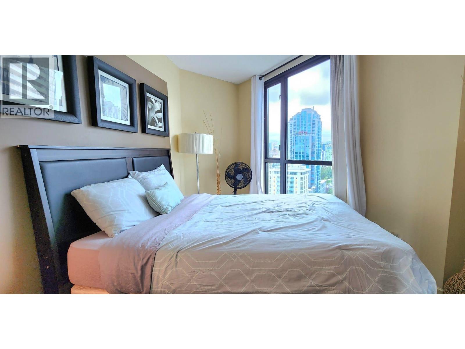 A bedroom with a large bed and a window overlooking a cityscape.