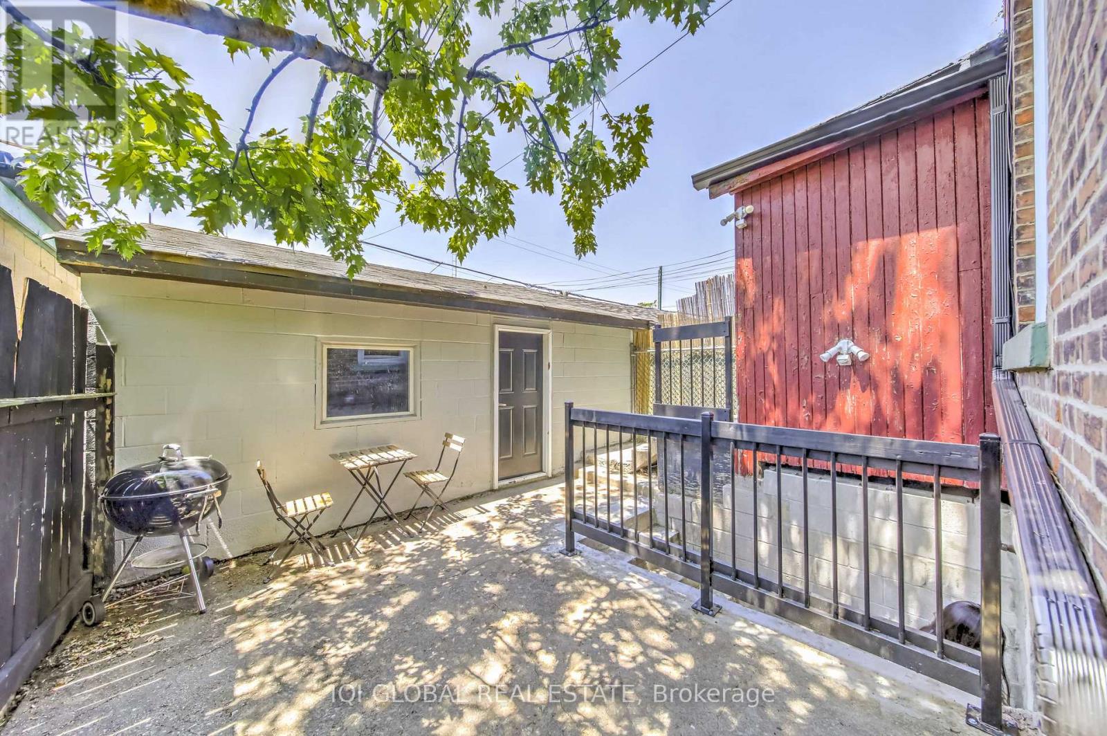 A patio with a grill and chairs is surrounded by a black fence.