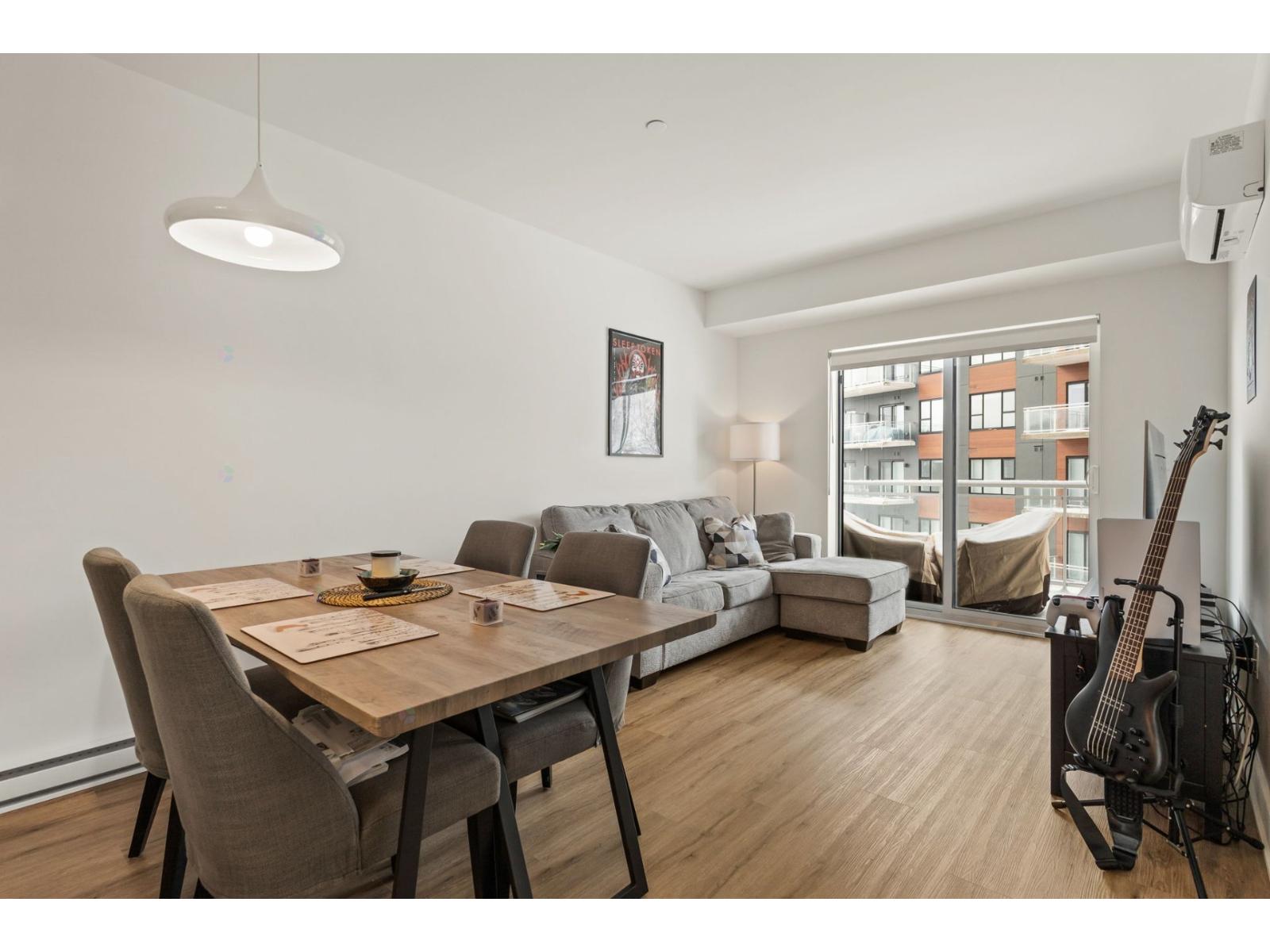 A modern living room with a wooden dining table and chairs, a couch, a guitar, and a window overlooking a building.