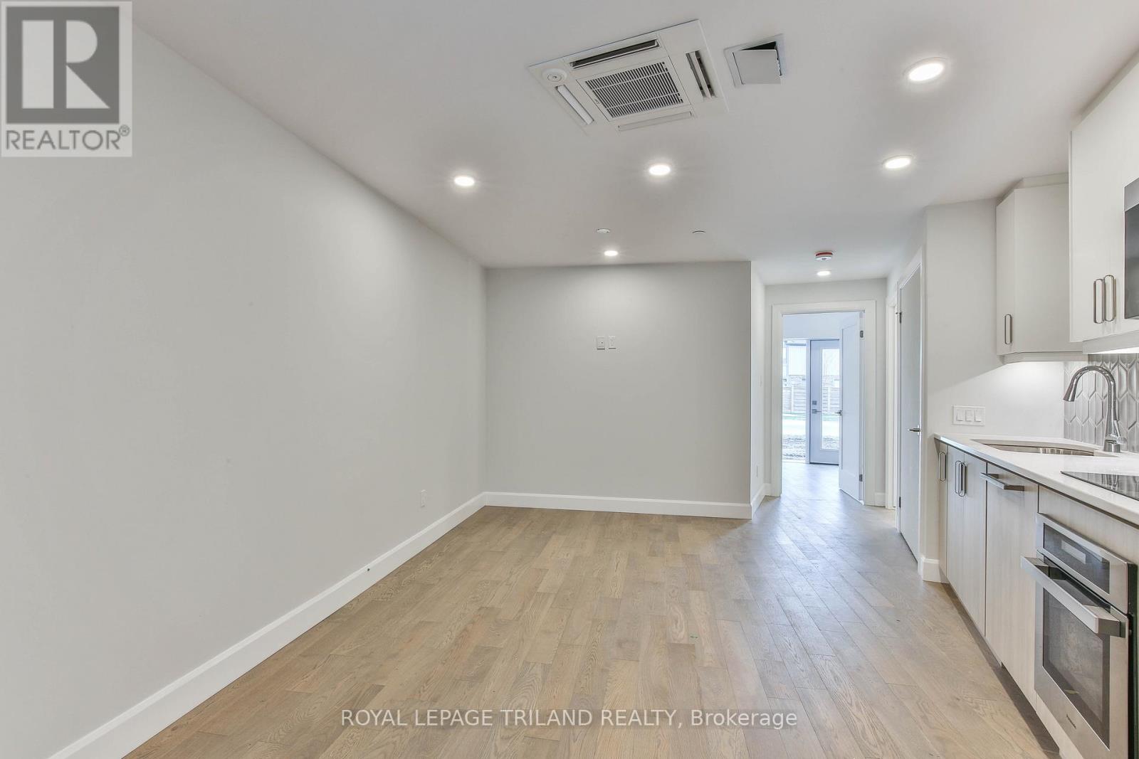 A spacious, empty room with wooden flooring and white walls.