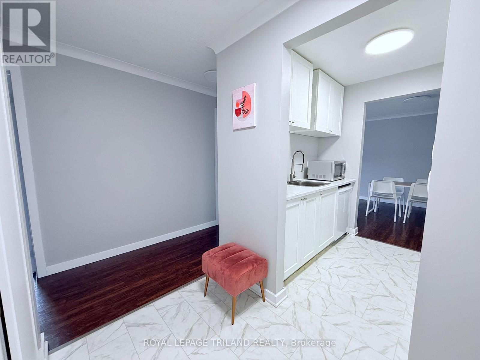 A white room with a red stool and a kitchen area.