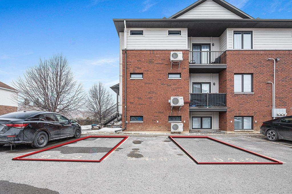 A black car is parked in a red outlined space in front of a brick building.