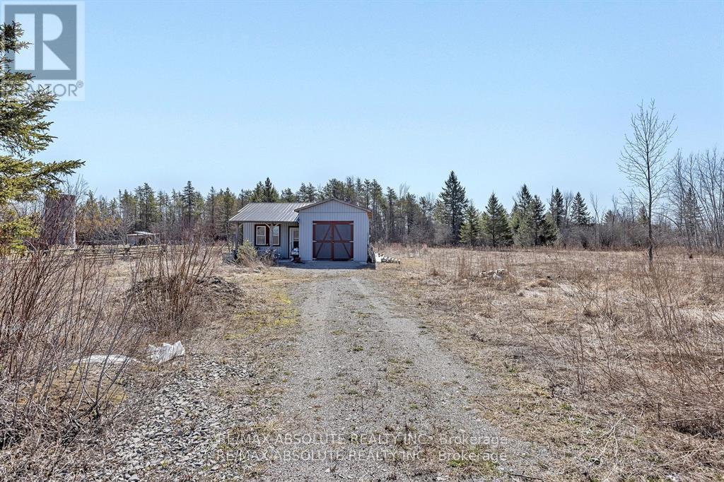 A small house is situated in a field with a dirt road leading to it.