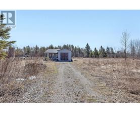 A small house is situated in a field with a dirt road leading to it.