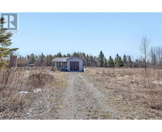 A small house is situated in a field with a dirt road leading to it.