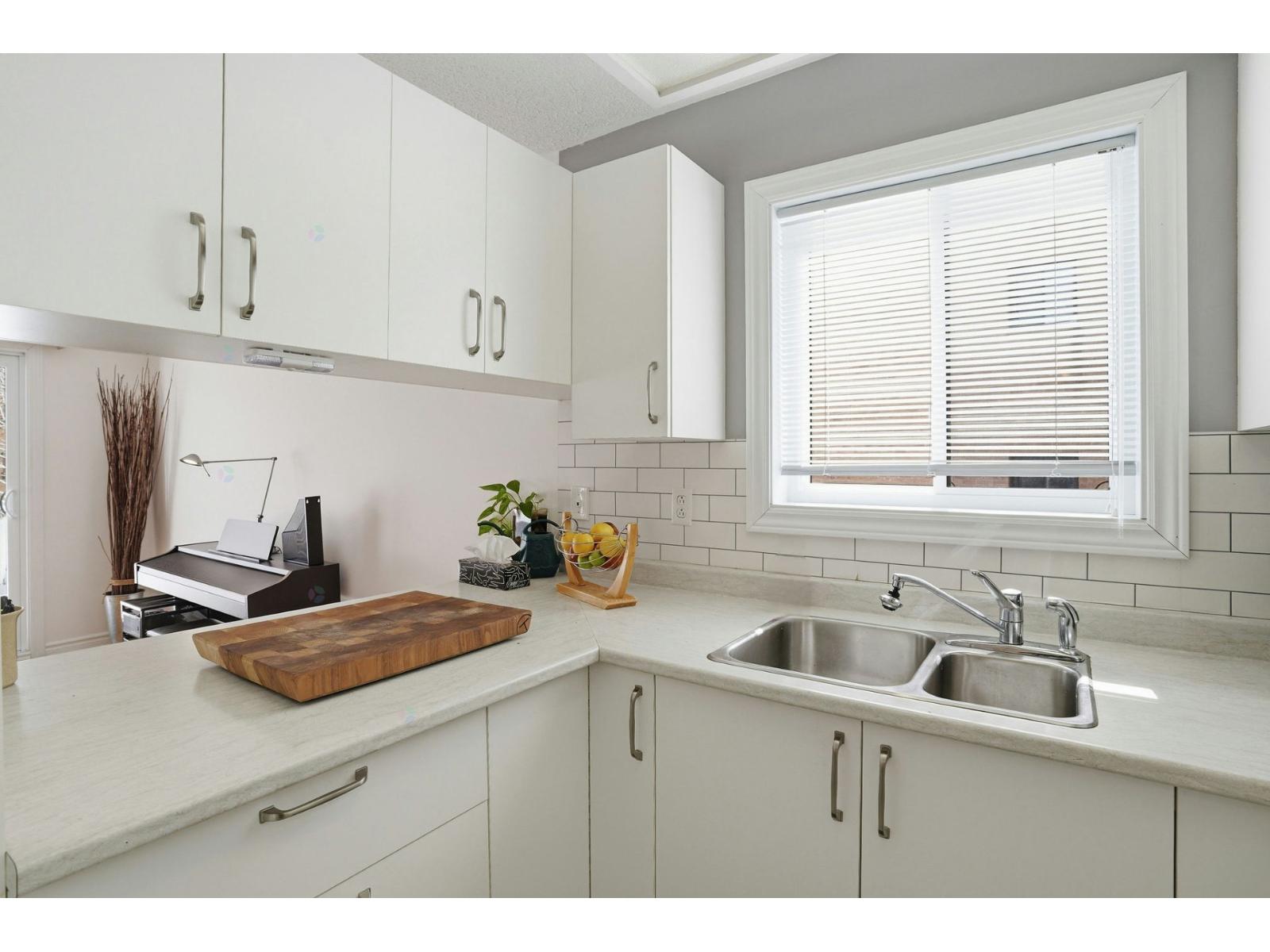 A kitchen with white cabinets and a window with blinds.