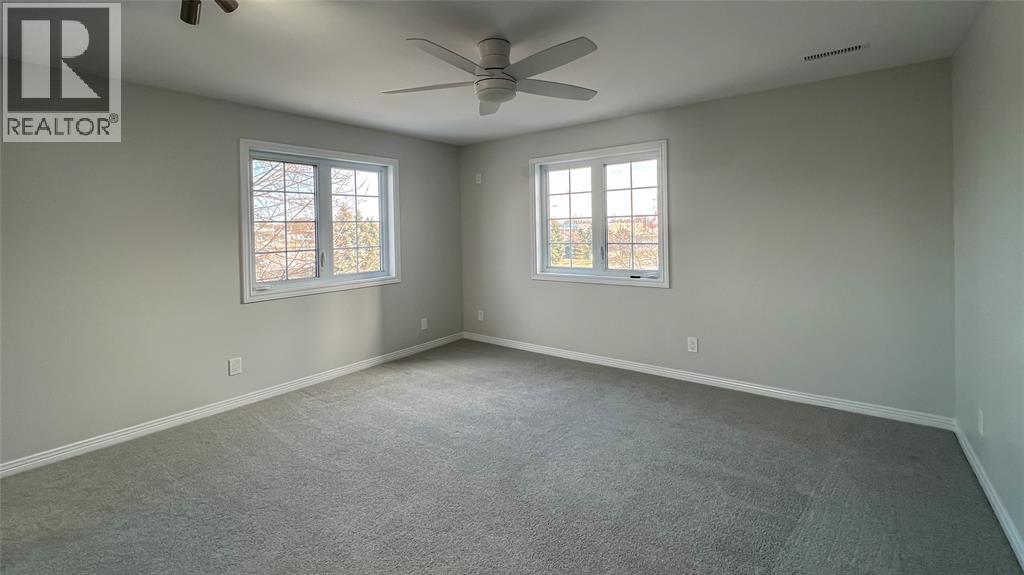 A spacious room with a ceiling fan and two windows.