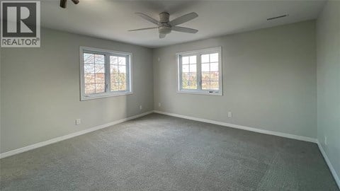 A spacious room with a ceiling fan and two windows.