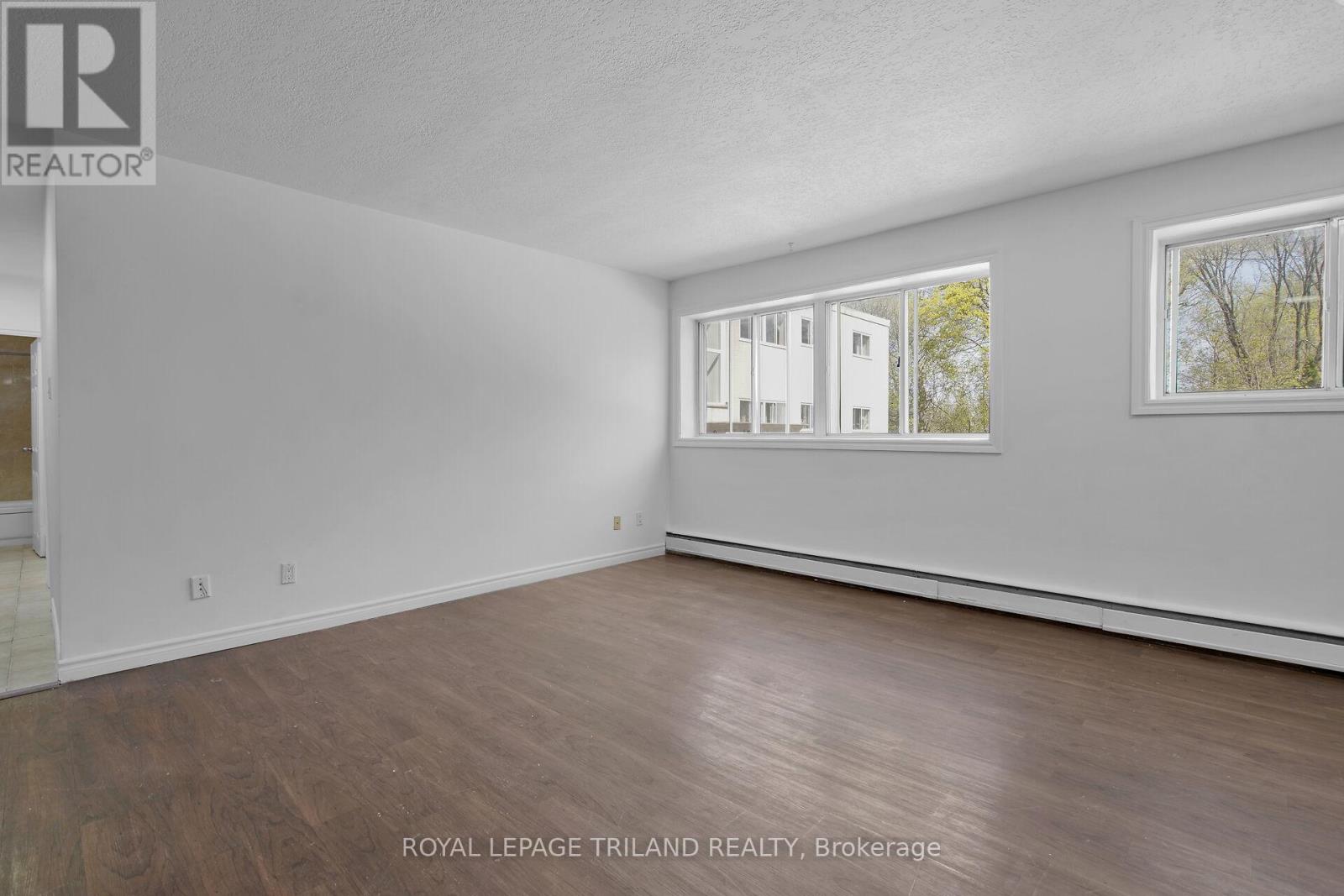 A white room with wood flooring and a window showing a building outside.