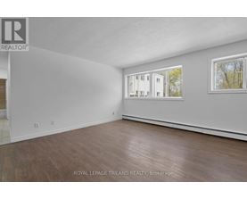 A white room with wood flooring and a window showing a building outside.