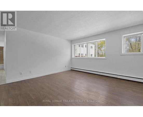 A white room with wood flooring and a window showing a building outside.