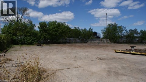 A large, empty, dirt field with a few trees and a pole in the distance.