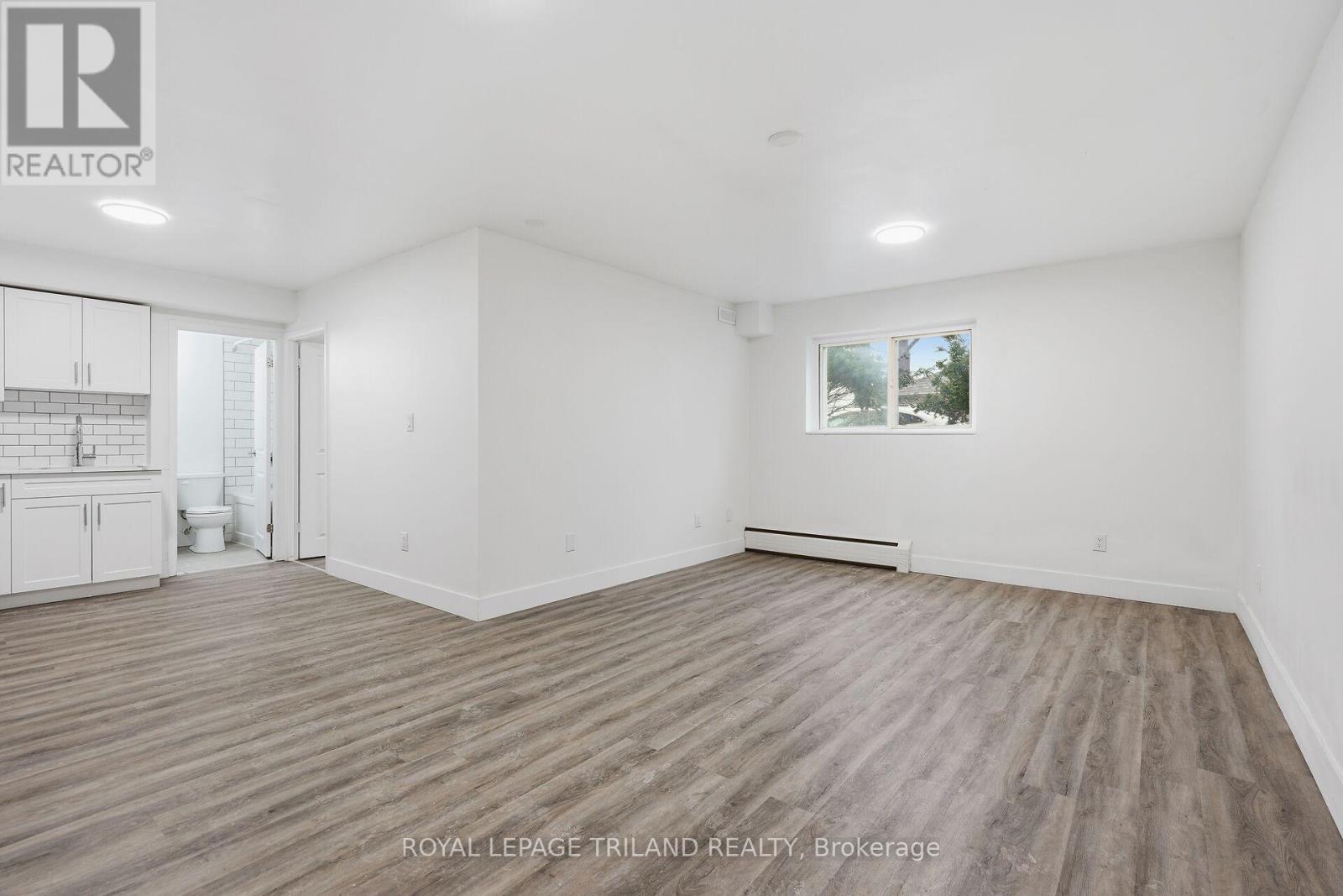A spacious room with wooden flooring and white walls, with a window showing a snowy landscape outside.
