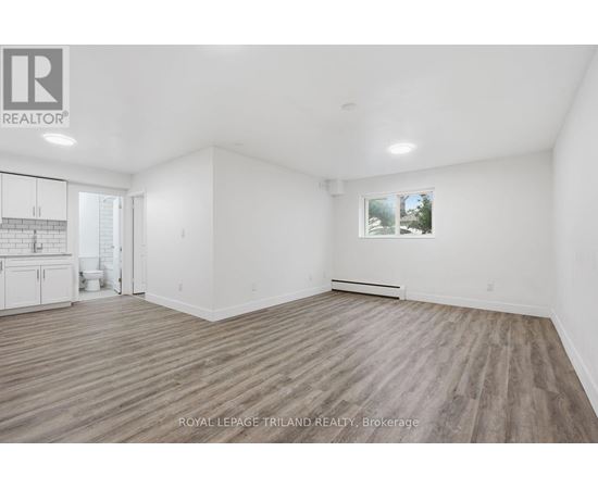 A spacious room with wooden flooring and white walls, with a window showing a snowy landscape outside.