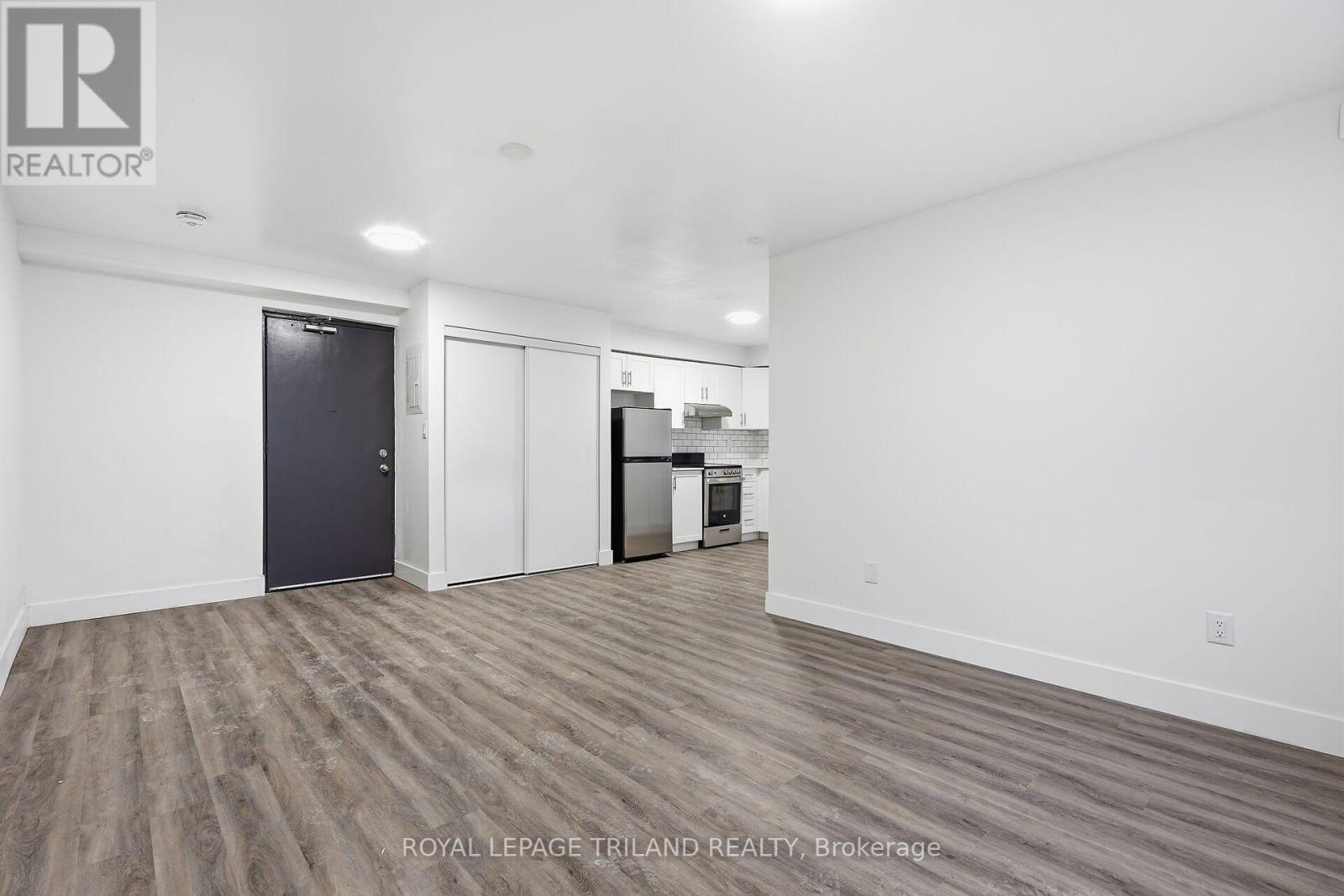 A spacious room with a door on the left and a kitchenette on the right.