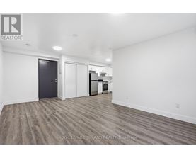 A spacious room with a door on the left and a kitchenette on the right.