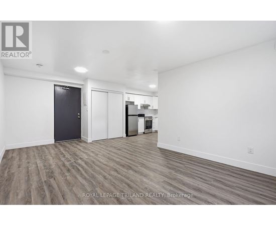 A spacious room with a door on the left and a kitchenette on the right.