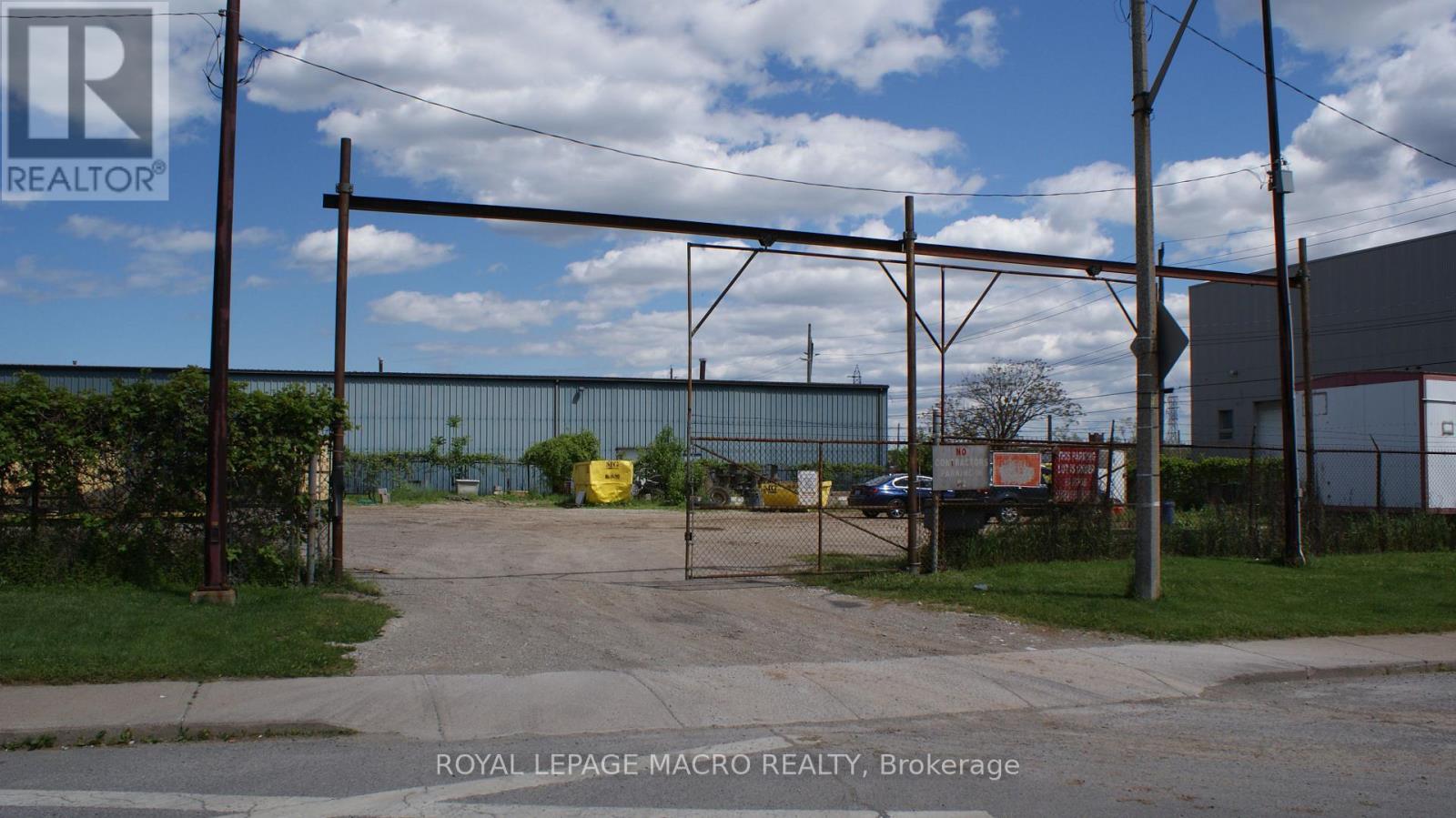 A sign for Royal LePage Macro Realty is in the foreground of an industrial area.