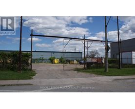 A sign for Royal LePage Macro Realty is in the foreground of an industrial area.