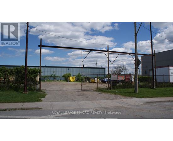 A sign for Royal LePage Macro Realty is in the foreground of an industrial area.
