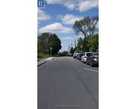 A street with cars parked on the side and a sign for Royal LePage Macro Realty in Brockville.