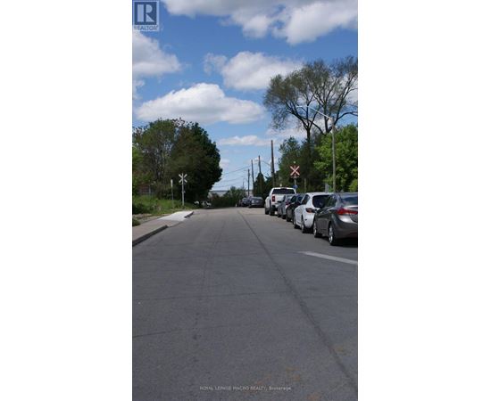 A street with cars parked on the side and a sign for Royal LePage Macro Realty in Brockville.
