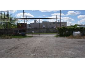 A gravel lot with a fence and a building in the background.