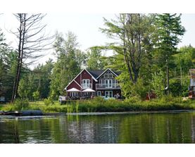 A house with a red roof is situated by a body of water.