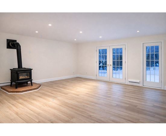 A wood stove is in a corner of a room with hardwood floors and white walls.