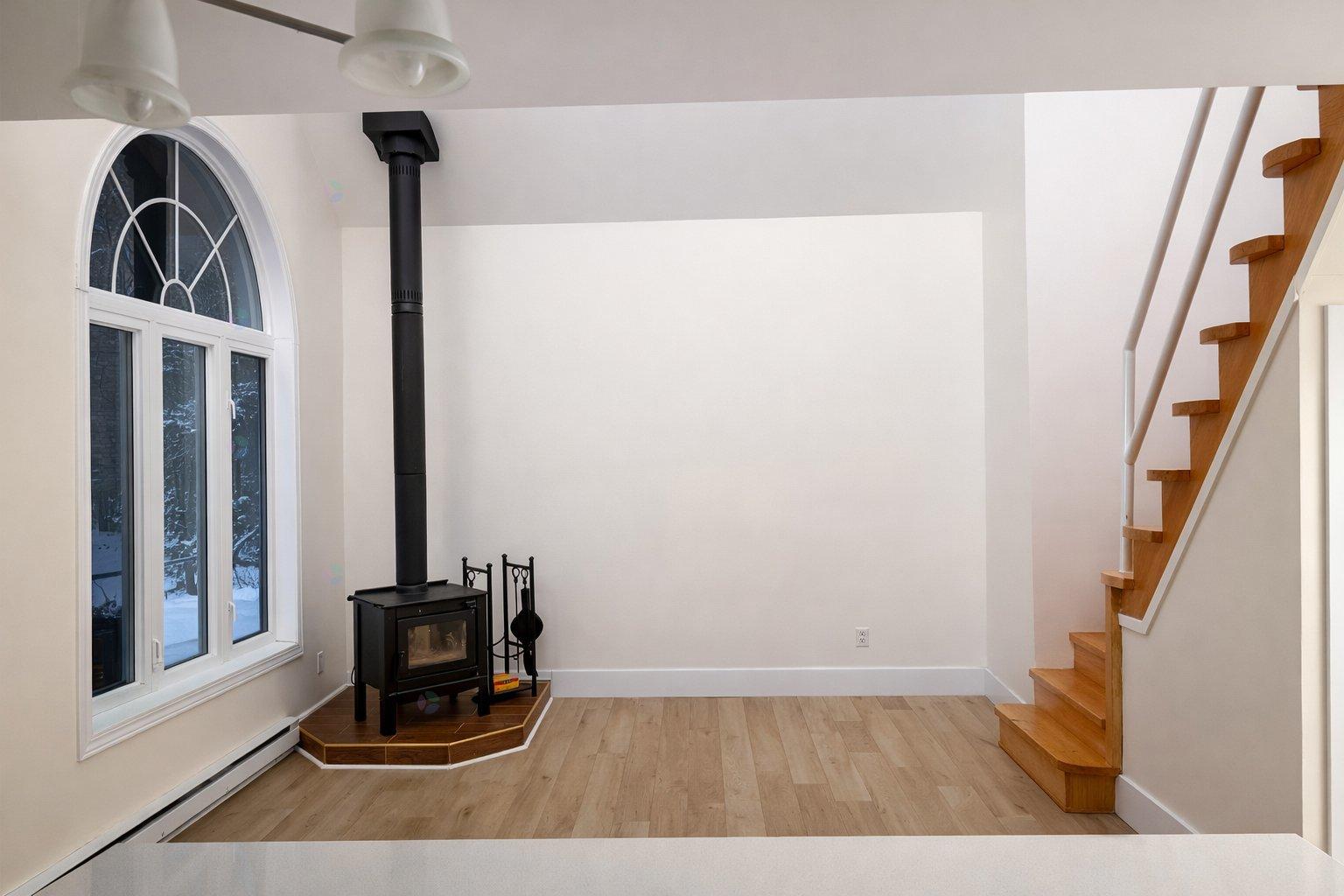 A wood burning stove in a white room with a staircase.