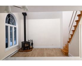 A wood burning stove in a white room with a staircase.