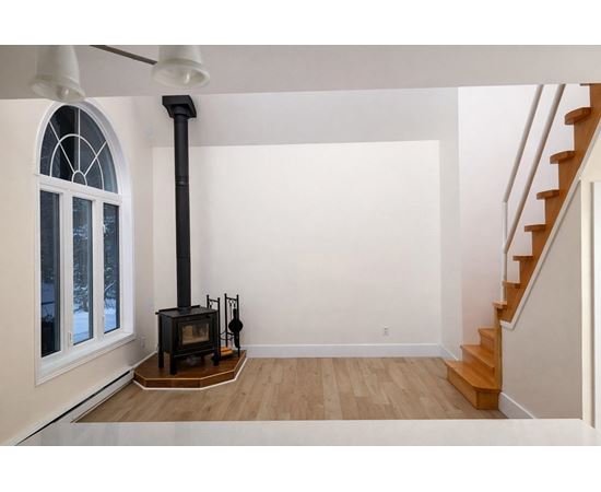 A wood burning stove in a white room with a staircase.