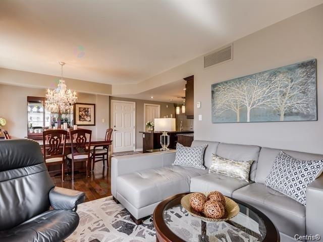 A living room with a black leather chair, a grey sofa, and a coffee table with a bowl of cookies on it.