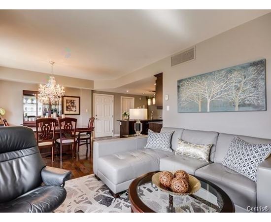 A living room with a black leather chair, a grey sofa, and a coffee table with a bowl of cookies on it.