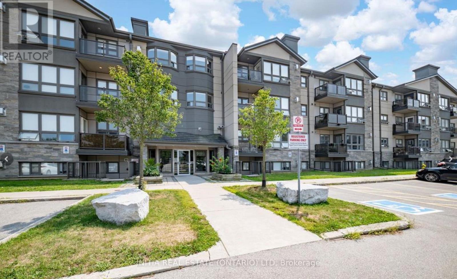 A large rock sits in the grass in front of a building with a REALTOR sign.