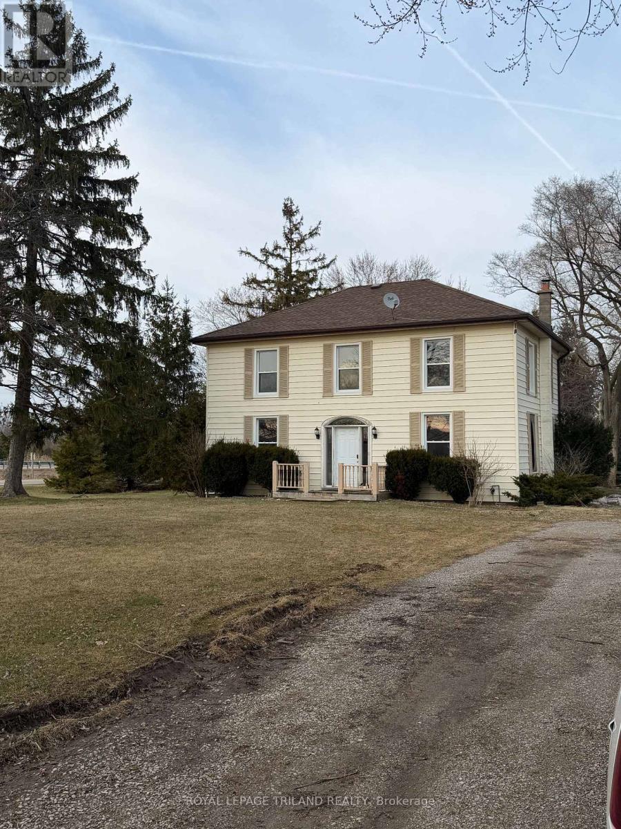 A house with a brown roof and white walls is surrounded by trees and bushes.